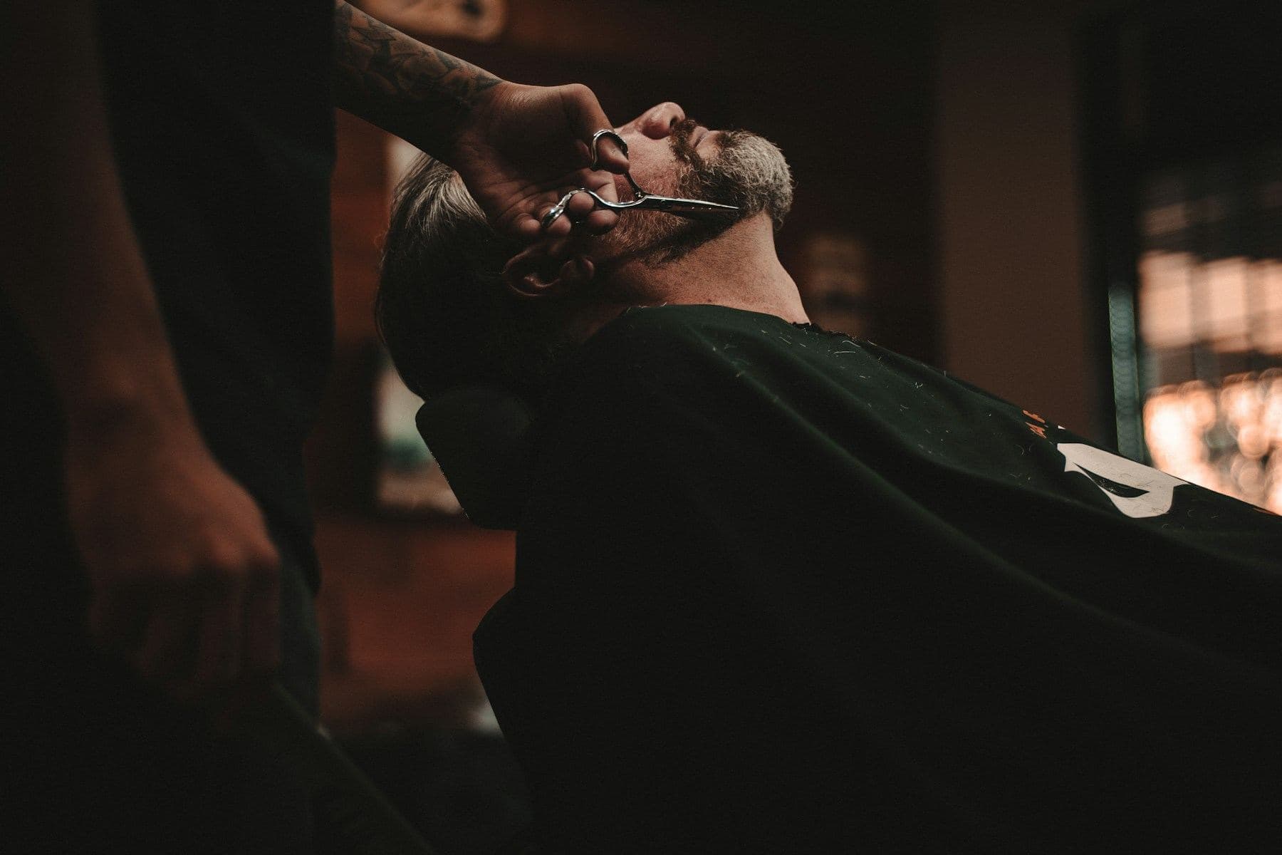 A barber trimming a client's beard with shears